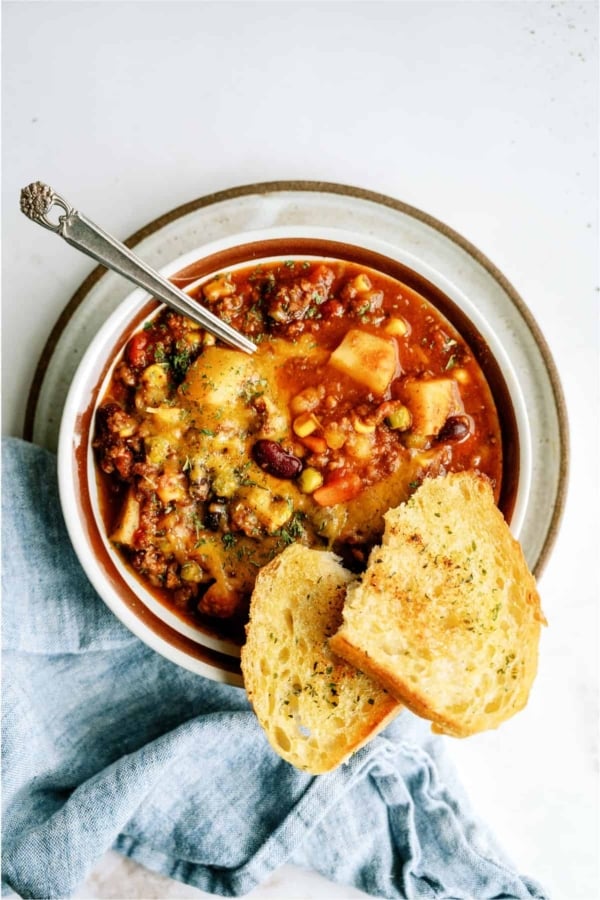 A bowl of shepherd's pie chili topped with herbs, served with a spoon and two slices of toasted bread on the side.