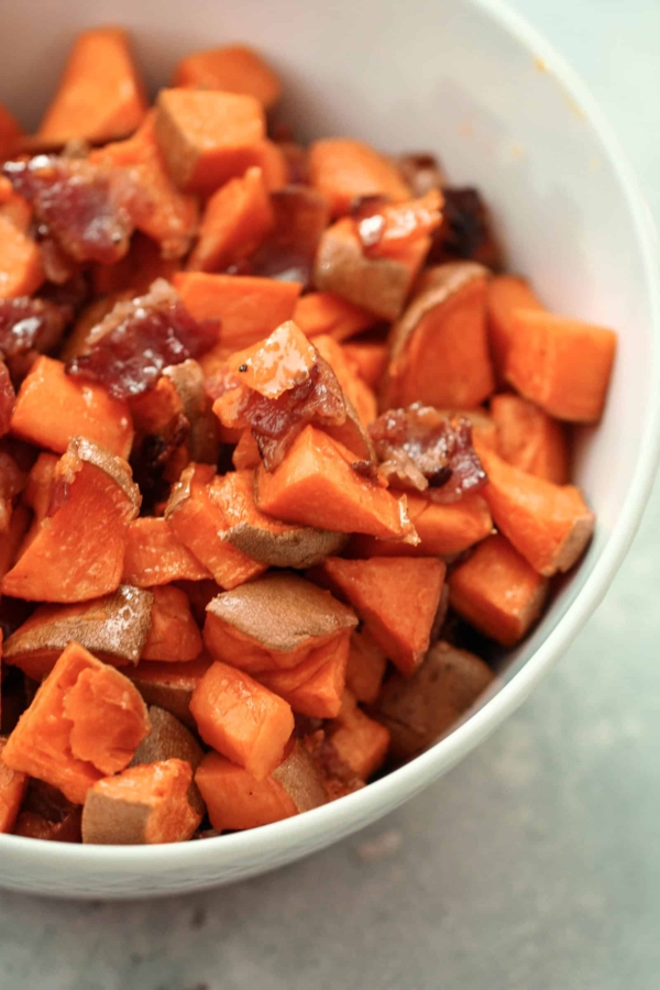 A bowl containing diced cooked sweet potatoes and pieces of dark-colored dates.