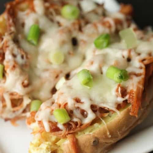 Baked potato topped with shredded meat, melted cheese, and chopped green onions on a white plate.