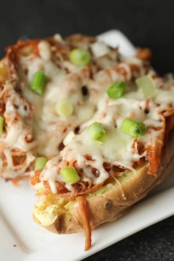 Baked potato topped with shredded meat, melted cheese, and chopped green onions on a white plate.