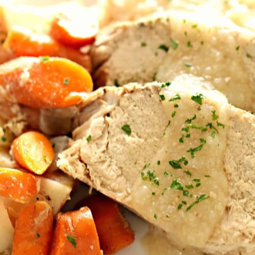Sliced pork roast topped with gravy, served with cooked carrots and potatoes on a white plate.