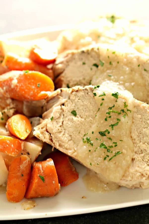 Sliced pork roast topped with gravy, served with cooked carrots and potatoes on a white plate.