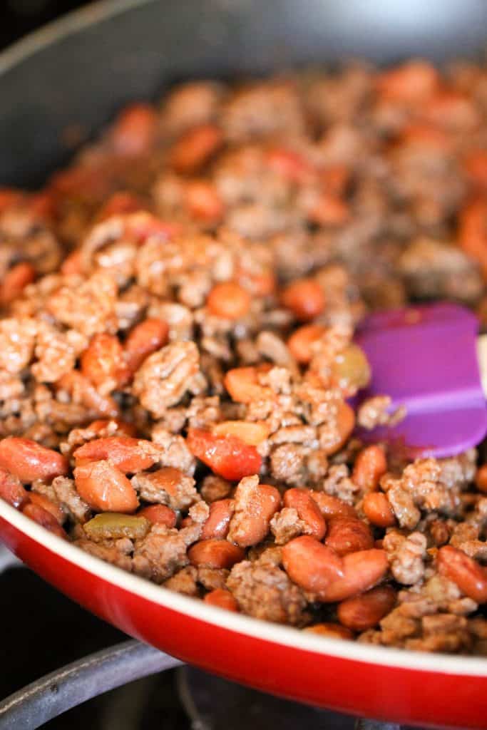 ground beef and beans cooking in a large skillet with purple spatula