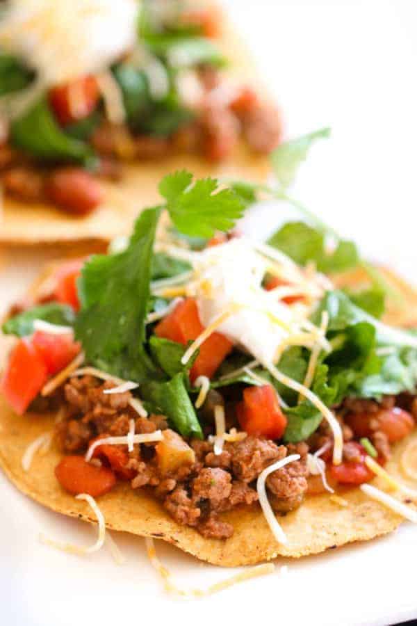 ground beef tostada topped with lettuce, tomato, sour cream, cheese, and cilantro