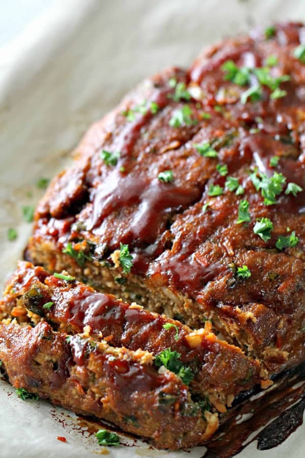 Sliced meatloaf topped with a glossy sauce and sprinkled with chopped parsley, resting on parchment paper.