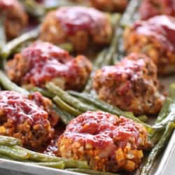Baked meatloaf muffins with green beans and tomato sauce on a baking sheet.