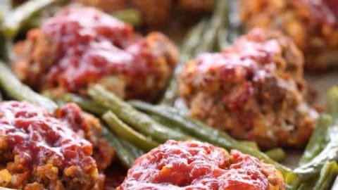 Baked meatloaf muffins with green beans and tomato sauce on a baking sheet.