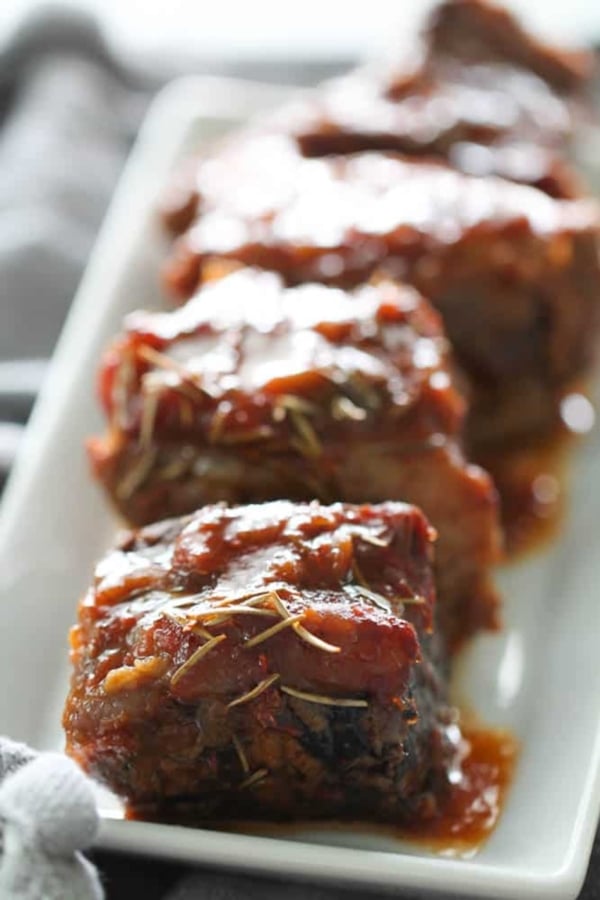 Close-up of glazed slow cooker short ribs garnished with herbs on a white platter.