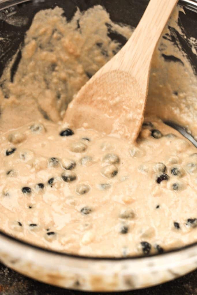 Mixing Protein Blueberry Muffin Batter in a mixing bowl with a wooden spoon.