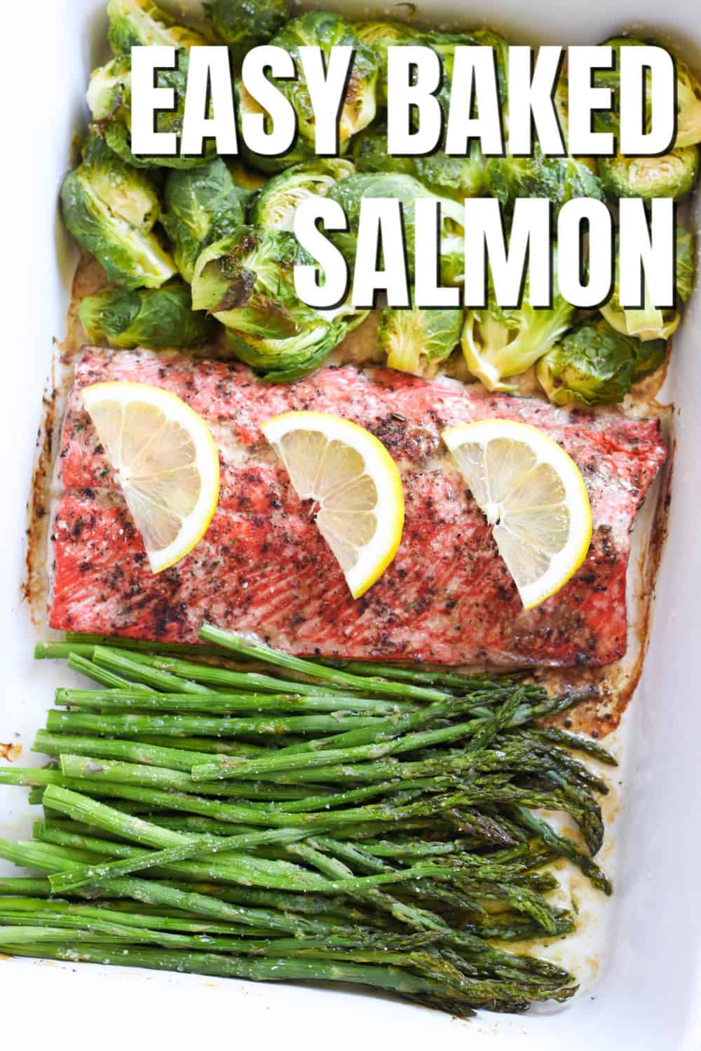 Baked salmon topped with lemons on a pan with brussels sprouts and asparagus