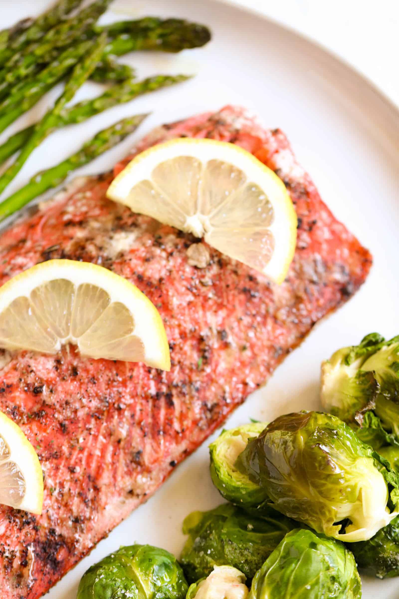 Baked salmon topped with lemons on a pan with brussels sprouts and asparagus