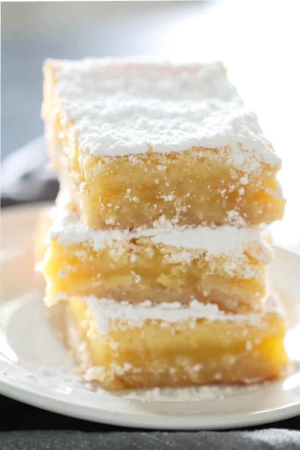 Lemon Bars stacked on plate topped with powdered sugar.