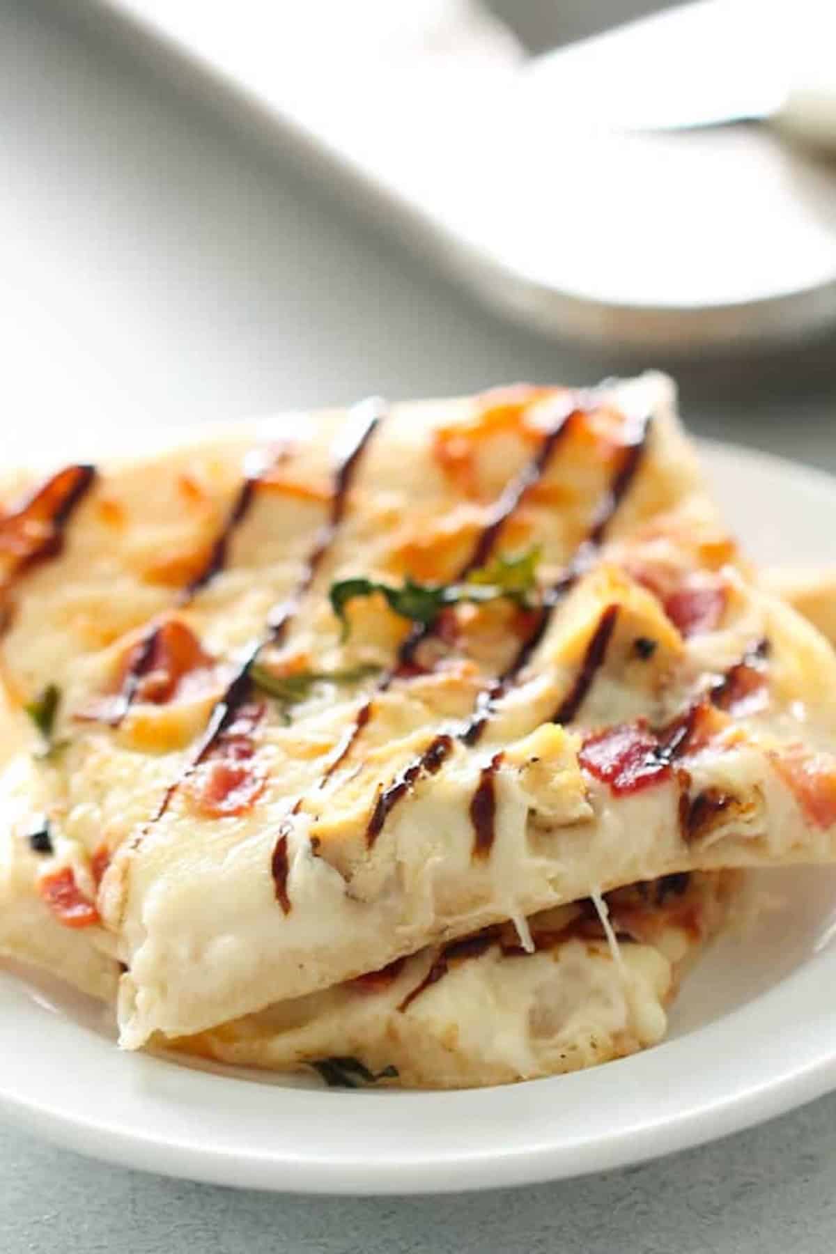 Two slices of pizza with melted cheese, sliced tomatoes, herbs, and a drizzle of balsamic glaze on a white plate.