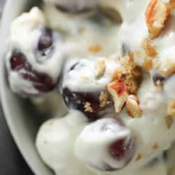 Close-up of a bowl containing grapes coated in creamy yogurt, topped with chopped pecans and a sprinkle of brown sugar.
