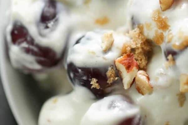 Close-up of a bowl containing grapes coated in creamy yogurt, topped with chopped pecans and a sprinkle of brown sugar.