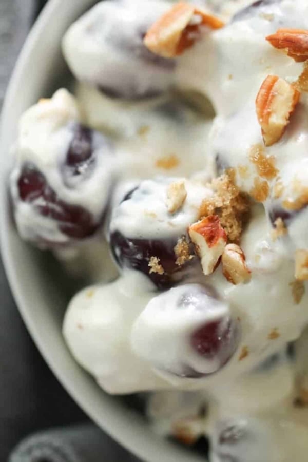 Close-up of a bowl containing grapes coated in creamy yogurt, topped with chopped pecans and a sprinkle of brown sugar.