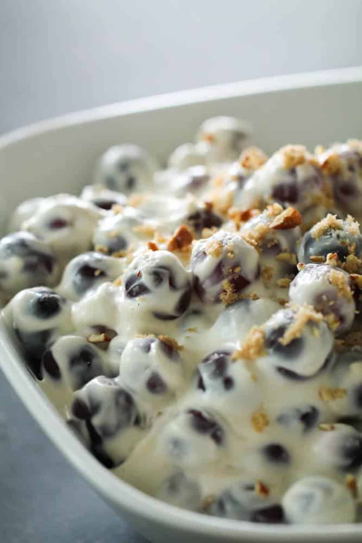 A close-up of a bowl filled with grapes coated in creamy dressing, topped with a sprinkle of crushed nuts or crumbs.