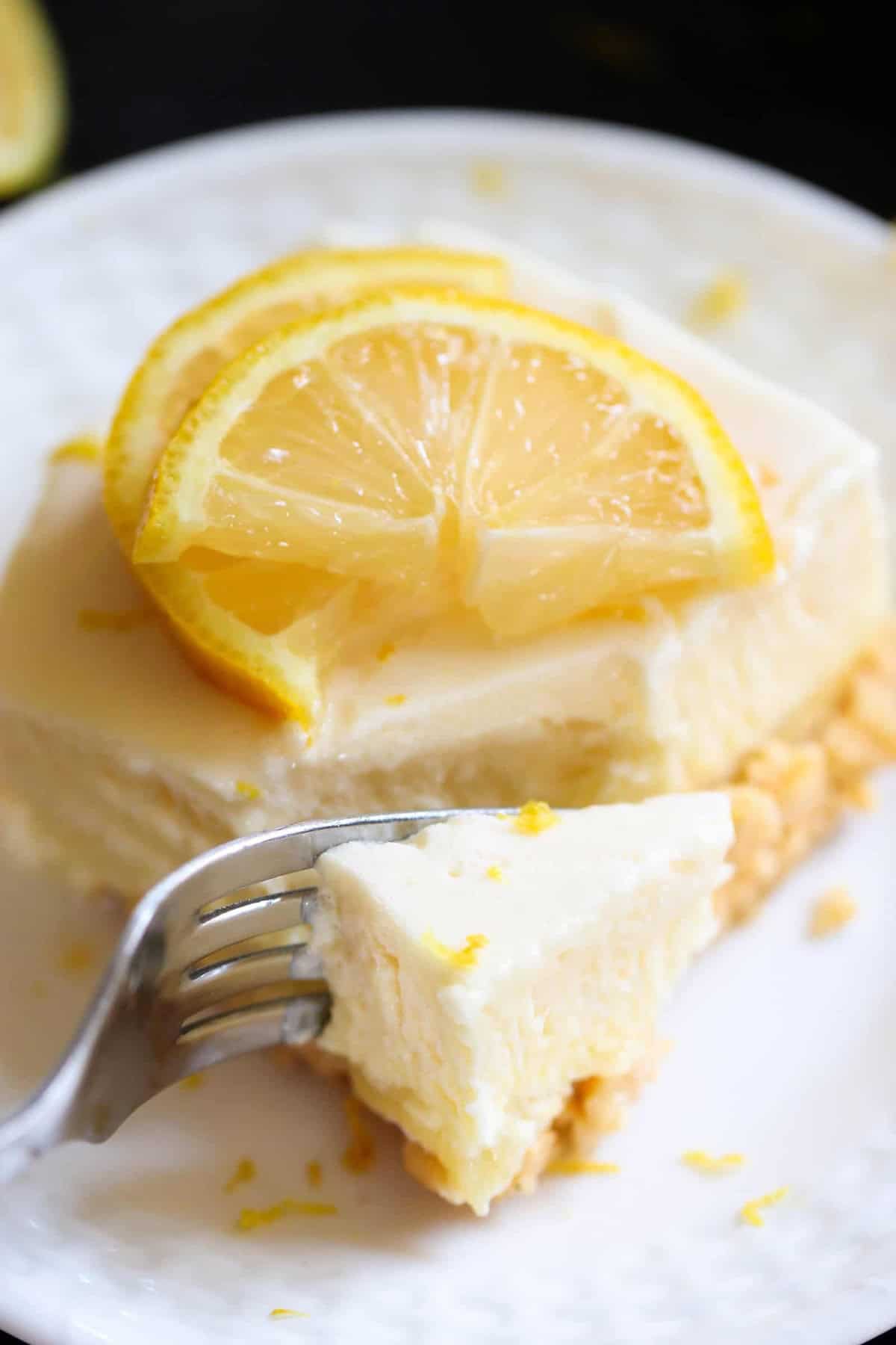 A slice of lemon fluff topped with lemon slices on a white plate, with a fork holding a bite-sized piece.