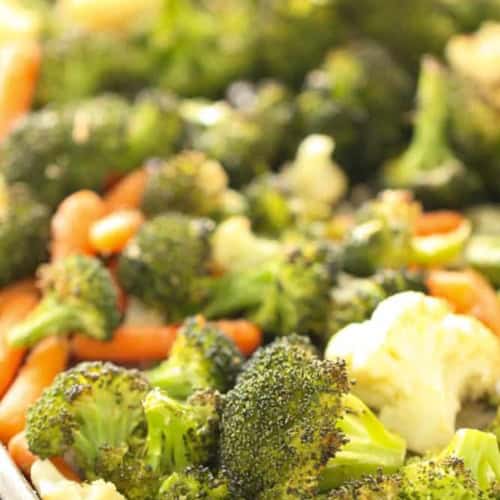 A close-up of a baking sheet filled with roasted broccoli, cauliflower, and baby carrots.