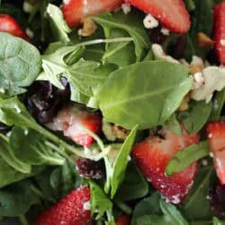 Close-up of a fresh salad with spinach, arugula, sliced strawberries, crumbled feta cheese, walnuts, and possibly dried cranberries.