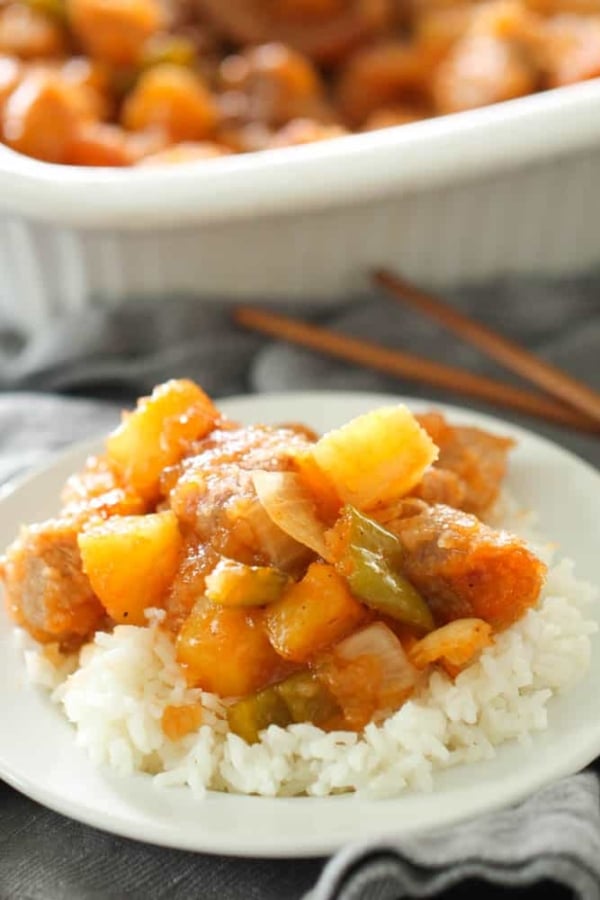 A plate with rice topped with a serving of Easy Baked Sweet and Sour Pork. With more Easy Baked Sweet and Sour Pork in the background.