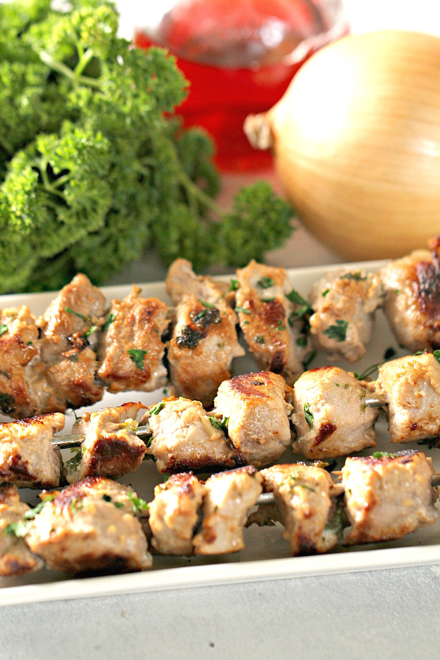 Mediterranean Pork Kabobs on a serving plate with vegetables in the back ground
