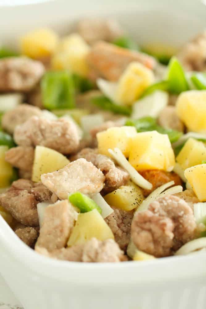 Lightly fried pieces of pork and fruits and veggies in a baking dish.