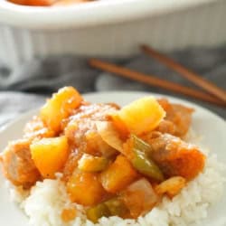 A plate with rice topped with a serving of Easy Baked Sweet and Sour Pork. With more Easy Baked Sweet and Sour Pork in the background.