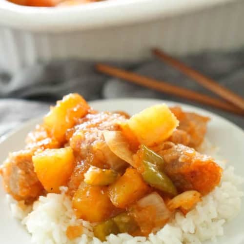 A plate with rice topped with a serving of Easy Baked Sweet and Sour Pork. With more Easy Baked Sweet and Sour Pork in the background.
