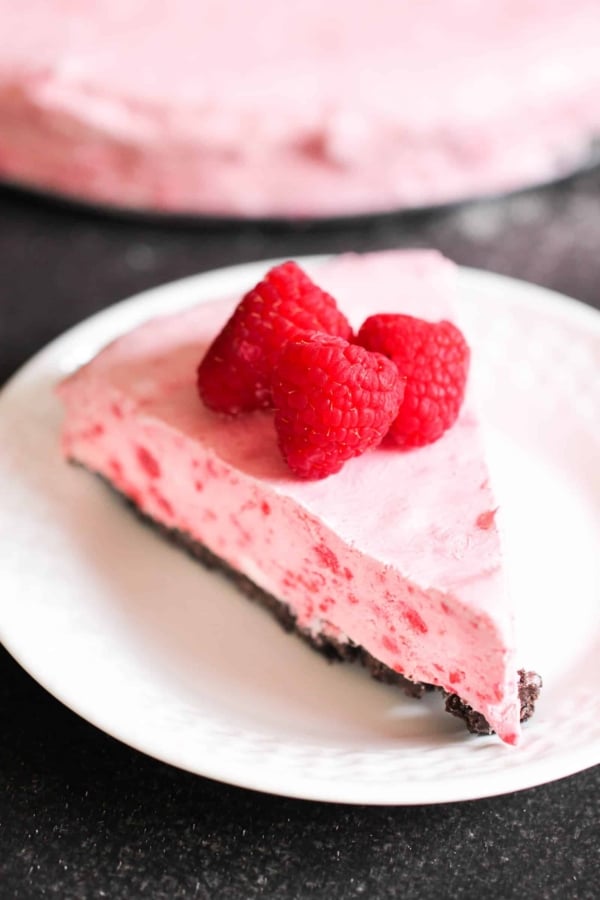 A slice of Frozen Raspberry Pie on a plate topped with fresh raspberries.