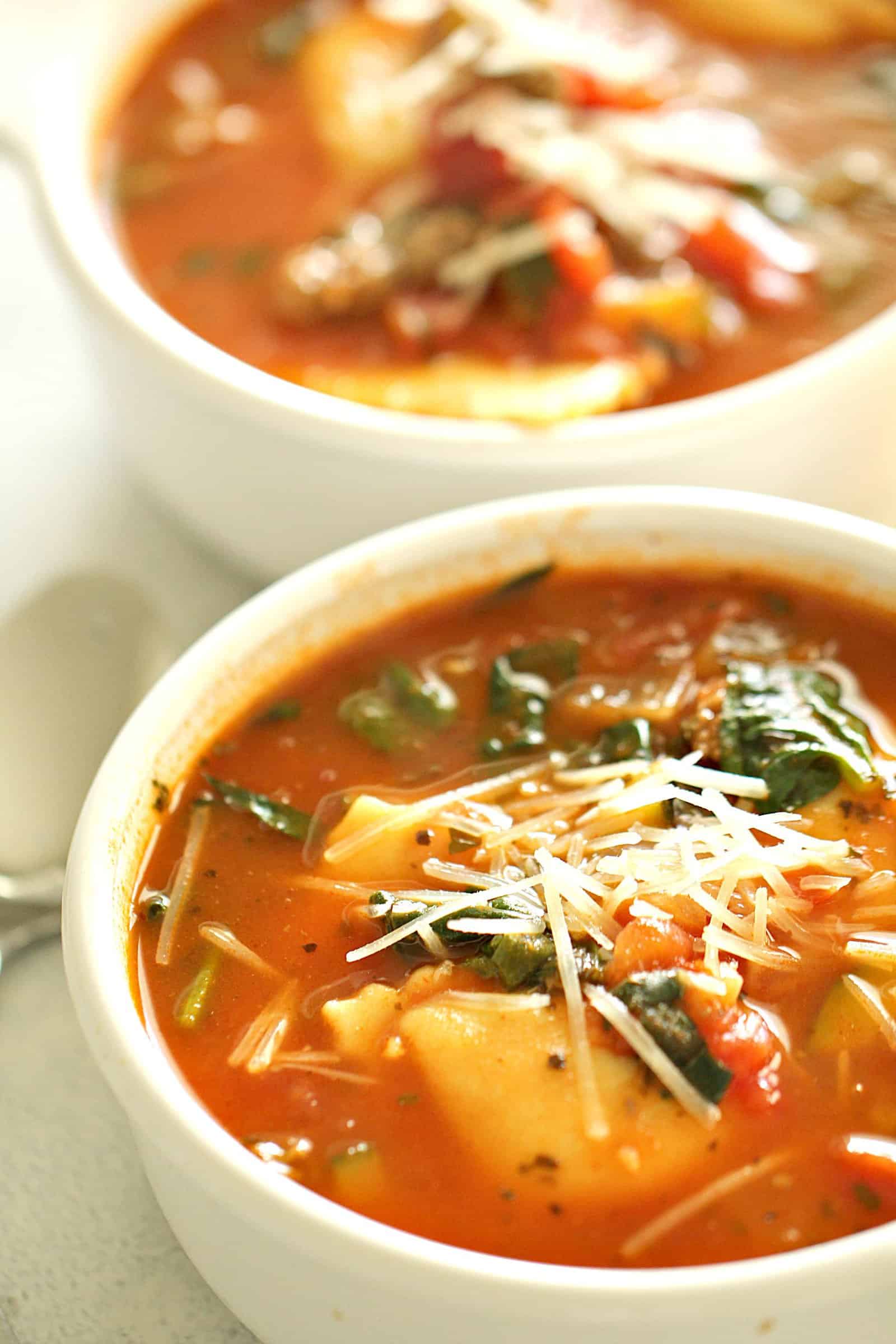 Ground Turkey Sausage Ravioli Soup in a white cup topped with cheese