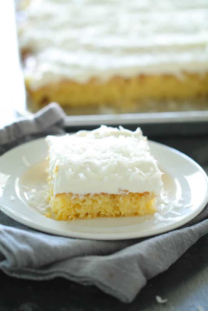 a slice of Sheet Pan Hawaiian Poke Cake with sprinkled coconut on a white plate