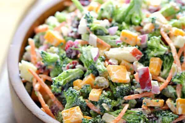A wooden bowl filled with chopped broccoli, carrots, cheese cubes, red onion, and diced apples mixed in a creamy dressing.