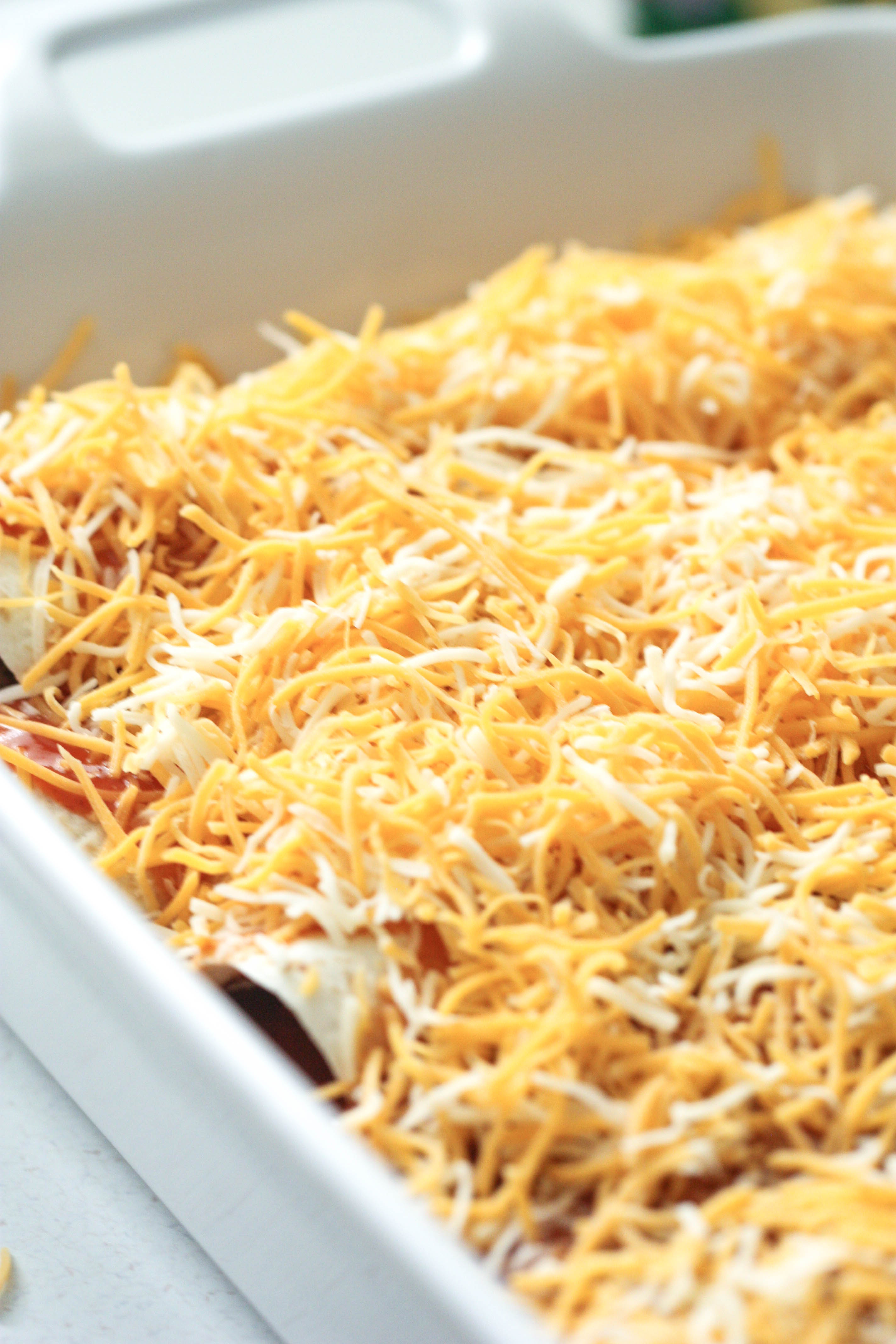 Enchiladas in a pan topped with cheese ready to bake