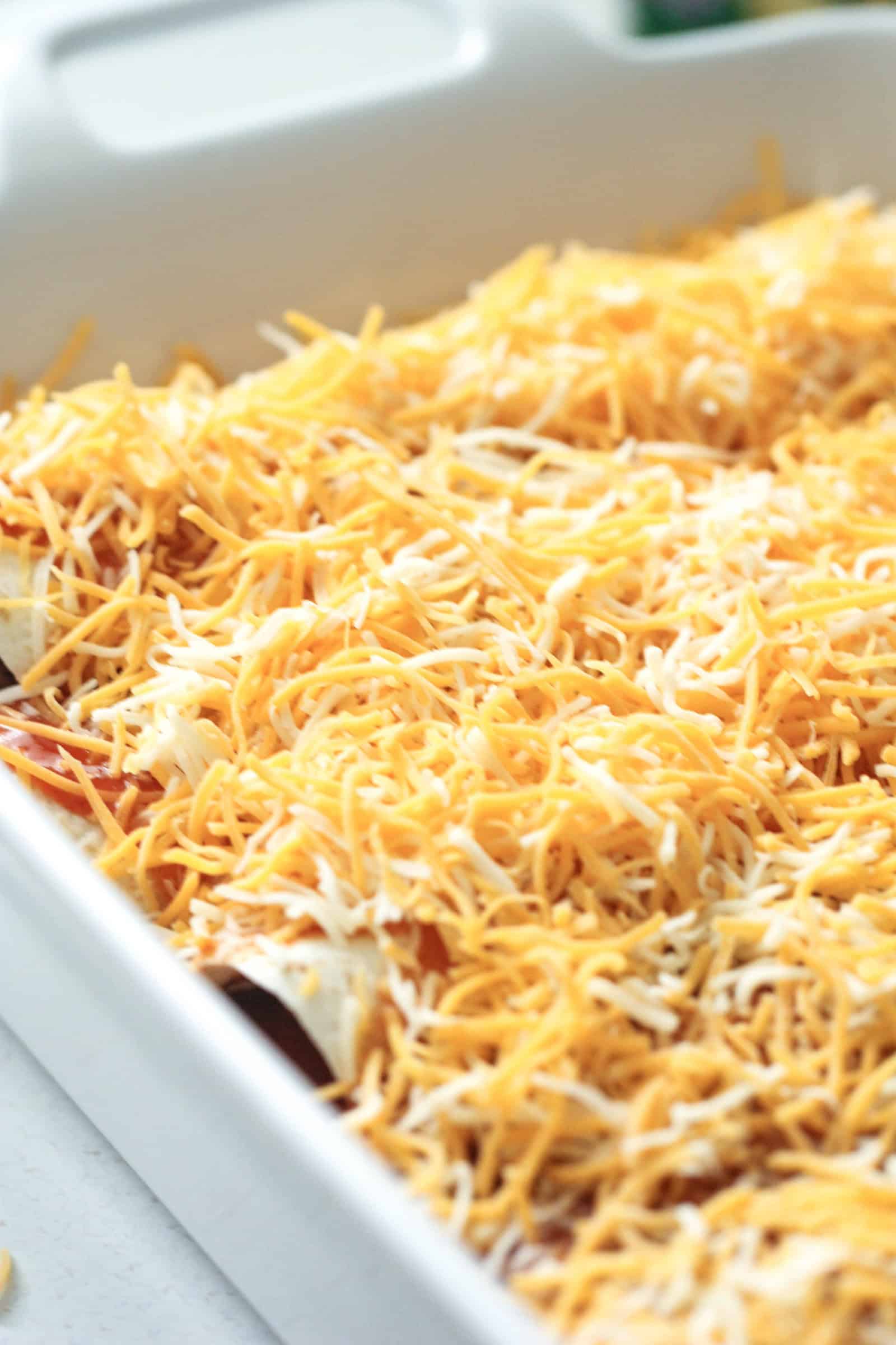 Enchiladas in a pan topped with cheese ready to bake