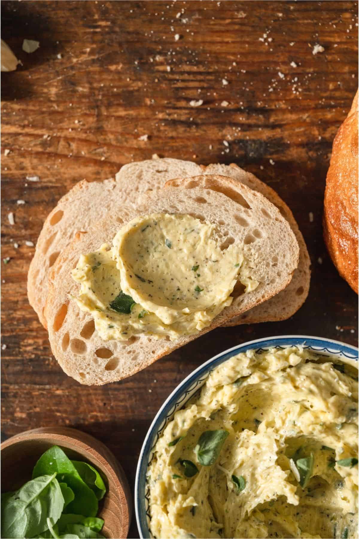 A slice of bread with some garlic butter on it and a bowl of Garlic Butter off to the side.