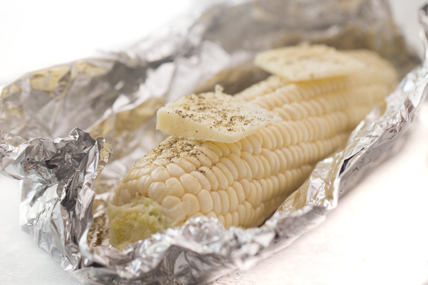 Corn on the cob wrapped in foil with butter and seasonings on it