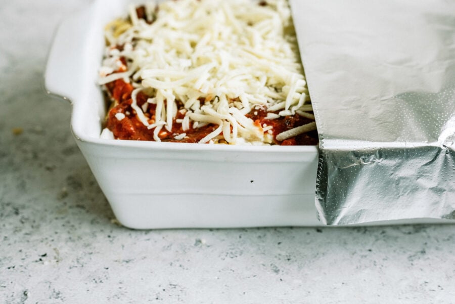 Spaghetti casserole topped with shredded cheese in casserole dish, covered with goil