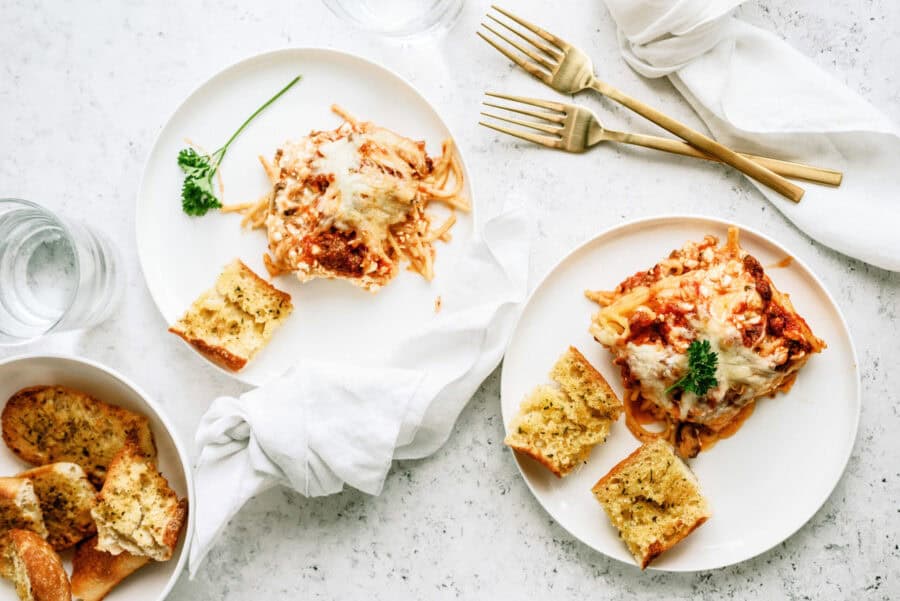 2 plates with servings of Baked Spaghetti and garlic bread on them