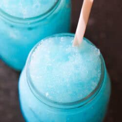 Two glass jars filled with bright blue slushy drinks, each with a white straw, viewed from above on a dark surface.