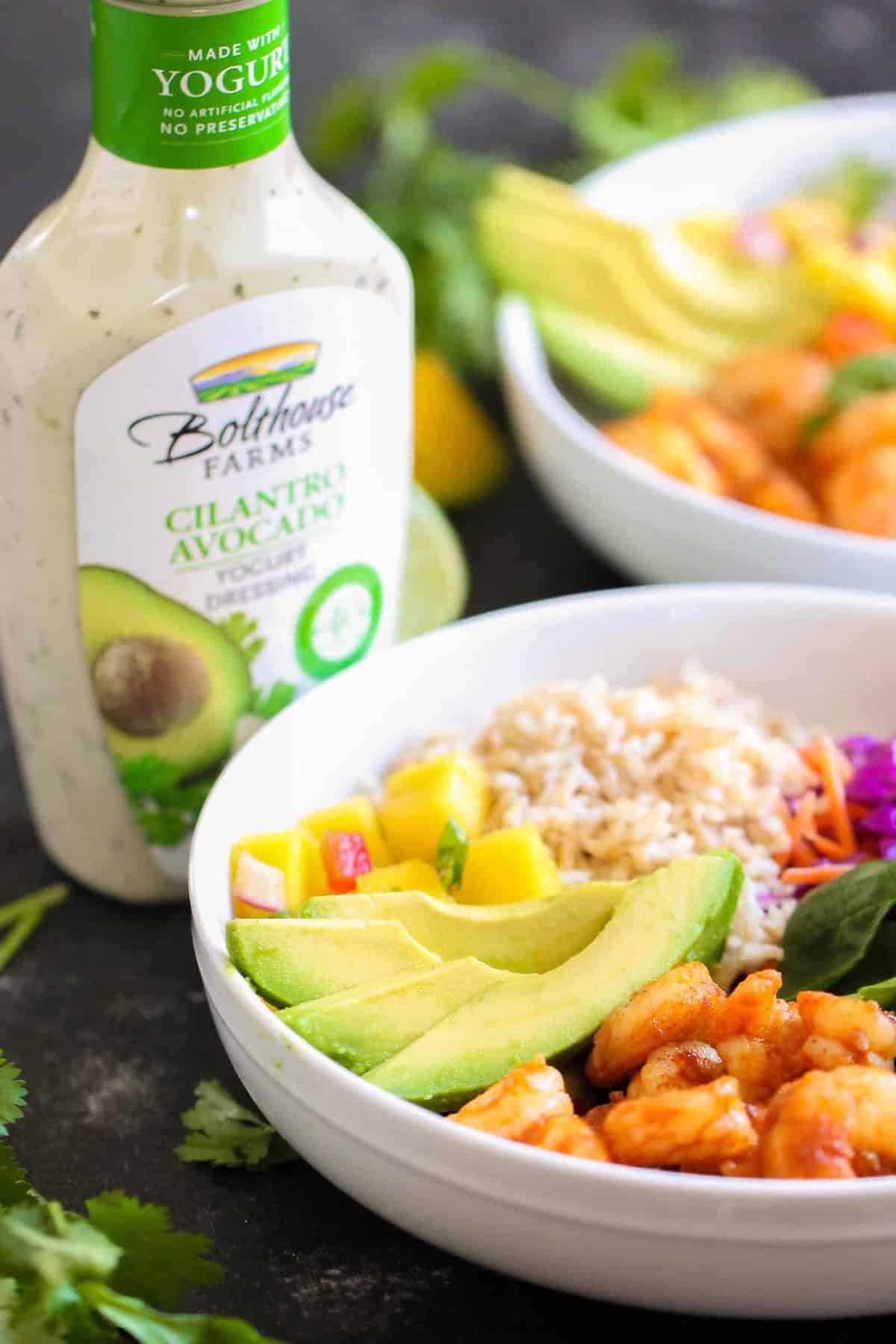 A bowl with rice, shrimp, avocado, and mango, next to a bottle of Bolthouse Farms Cilantro Avocado yogurt dressing.