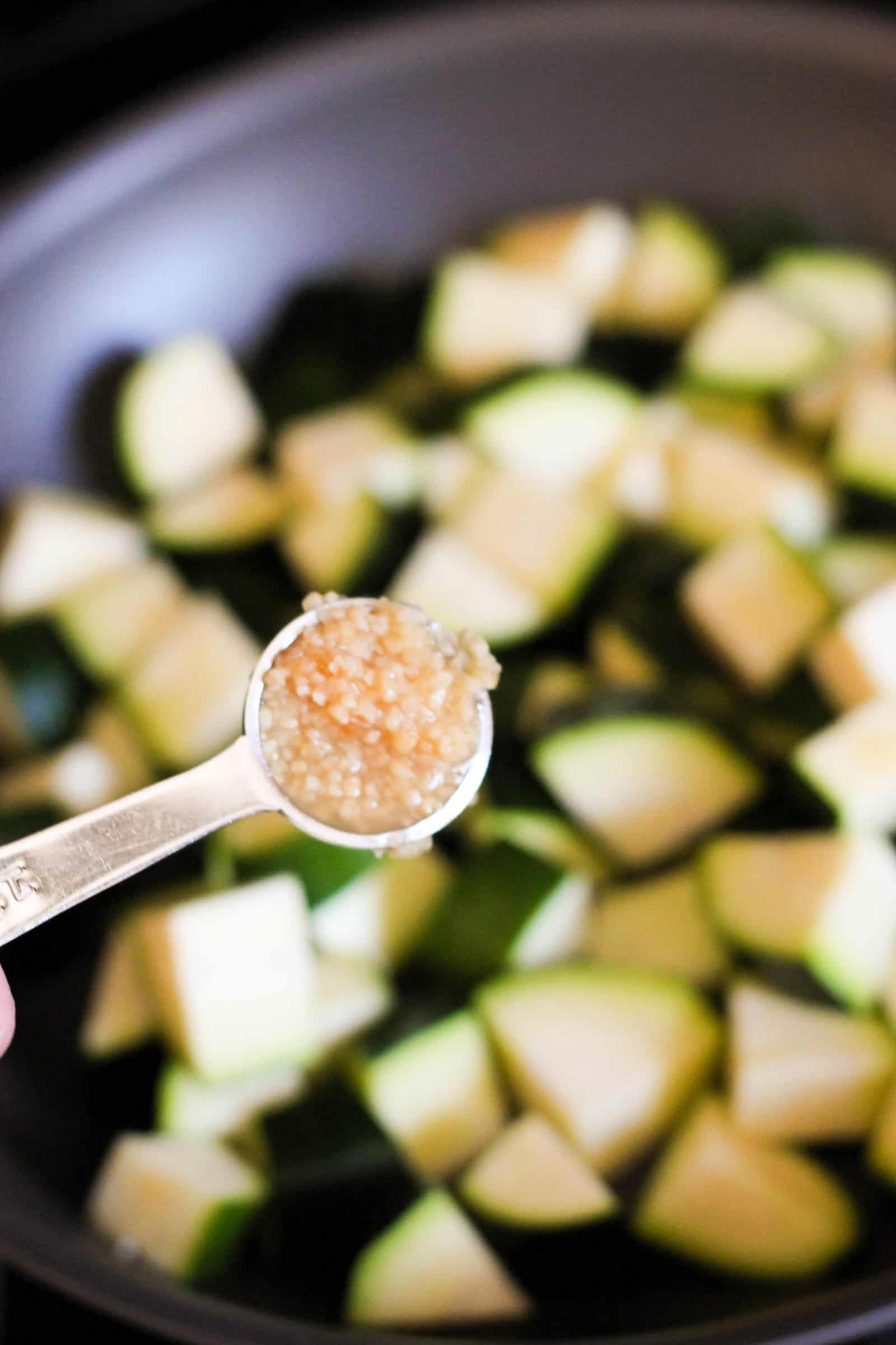 spoon full of garlic added to sliced zucchini in large skillet