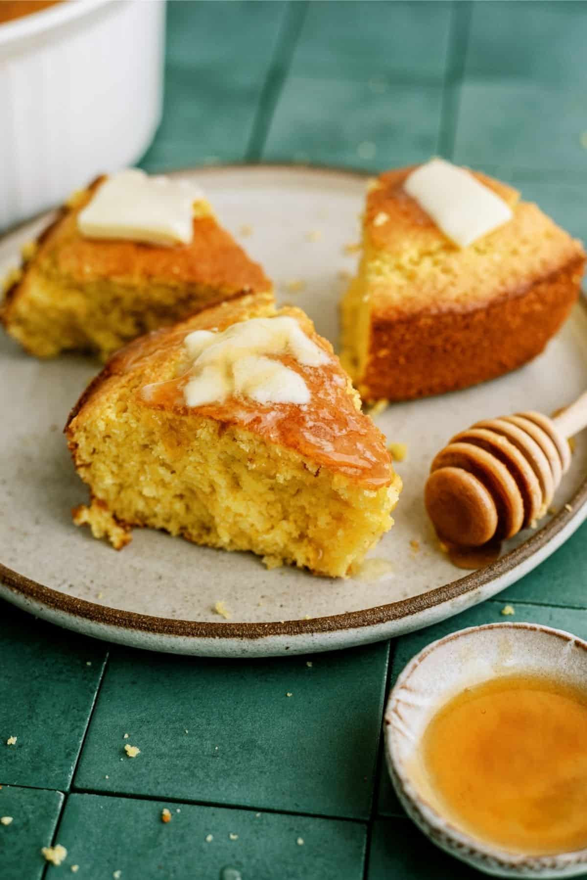 Easy Homemade Cornbread sliced on a plate, topped with butter and honey