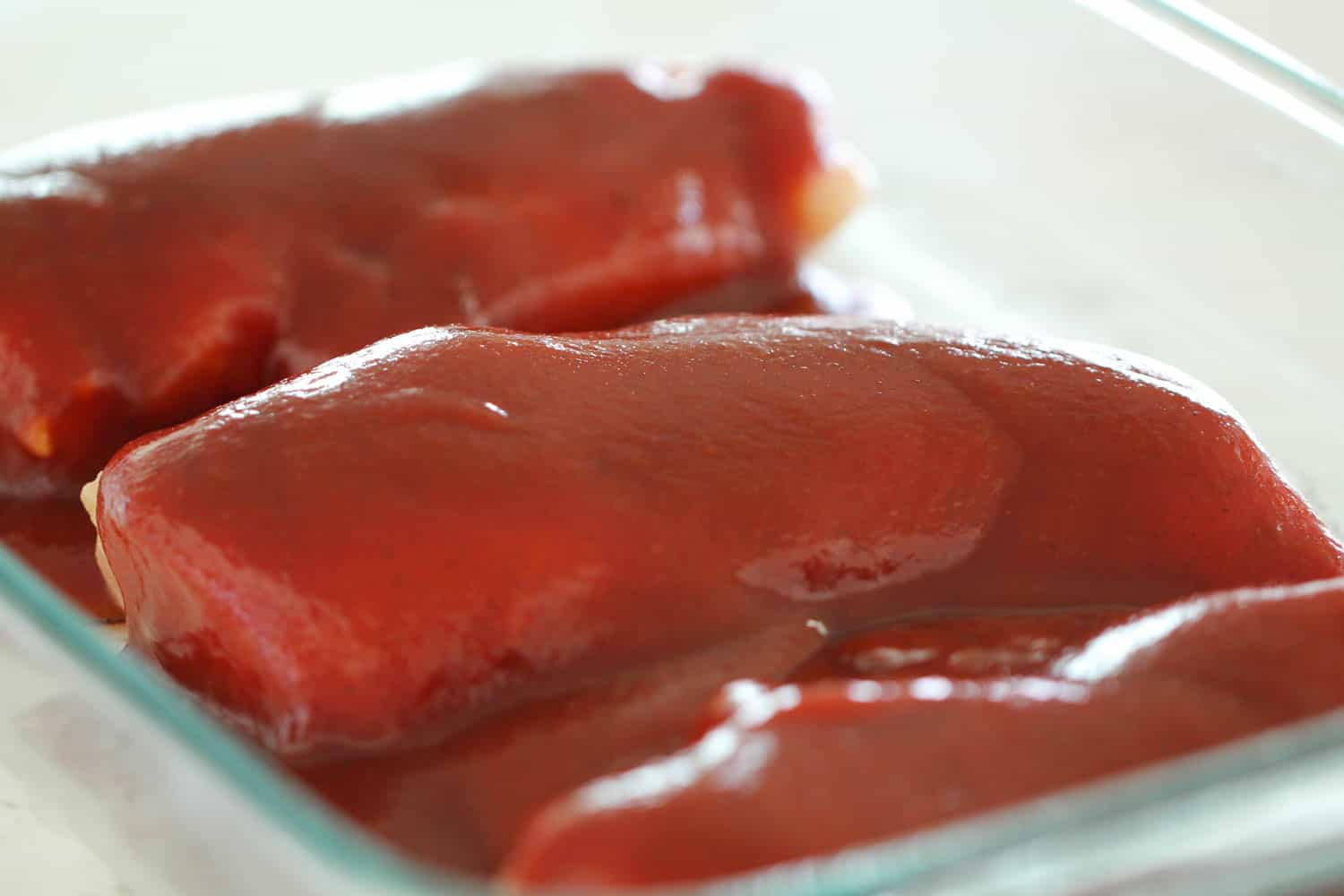 Chicken covered in BBQ sauce in baking dish