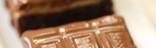A close-up of chocolate brownie squares topped with a layer of chocolate, arranged in a row on a white plate.
