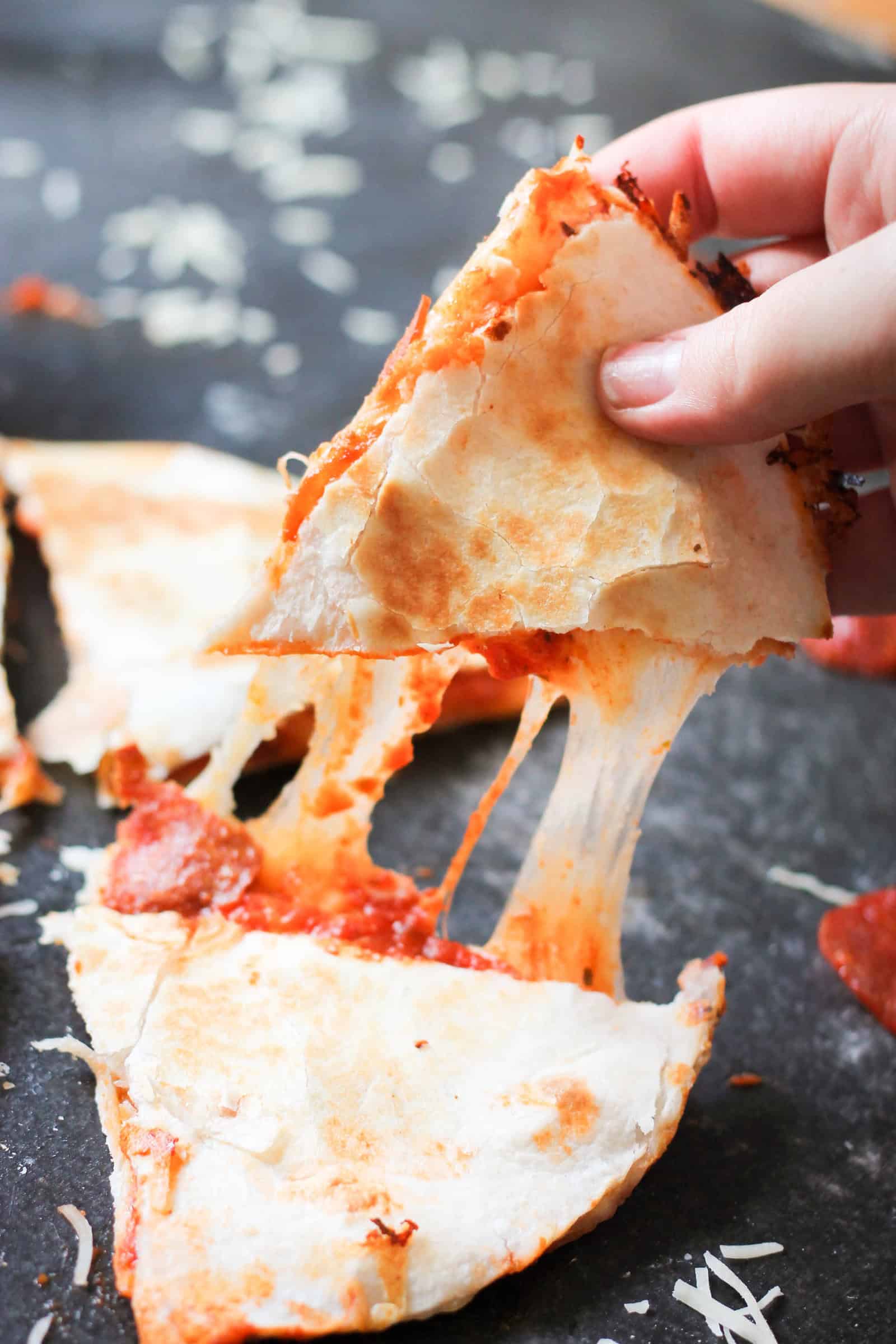 a triangle of easy pizza quesadillas being pulled apart to show gooey, melty cheese