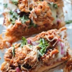 Close-up of barbecue chicken pizza topped with shredded chicken, melted cheese, red onions, barbecue sauce, and fresh cilantro on a foil-lined surface.