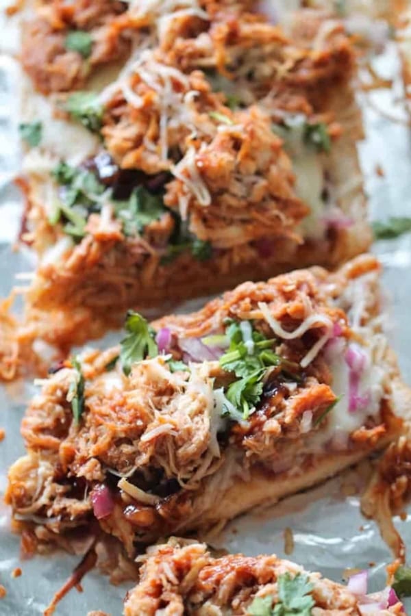 Close-up of barbecue chicken pizza topped with shredded chicken, melted cheese, red onions, barbecue sauce, and fresh cilantro on a foil-lined surface.