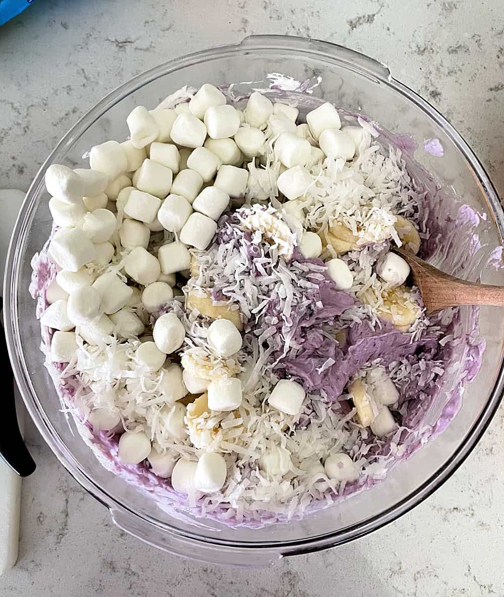 Ingredients for Blueberry Fluff Salad in a glass mixing bowl with a wooden spoon