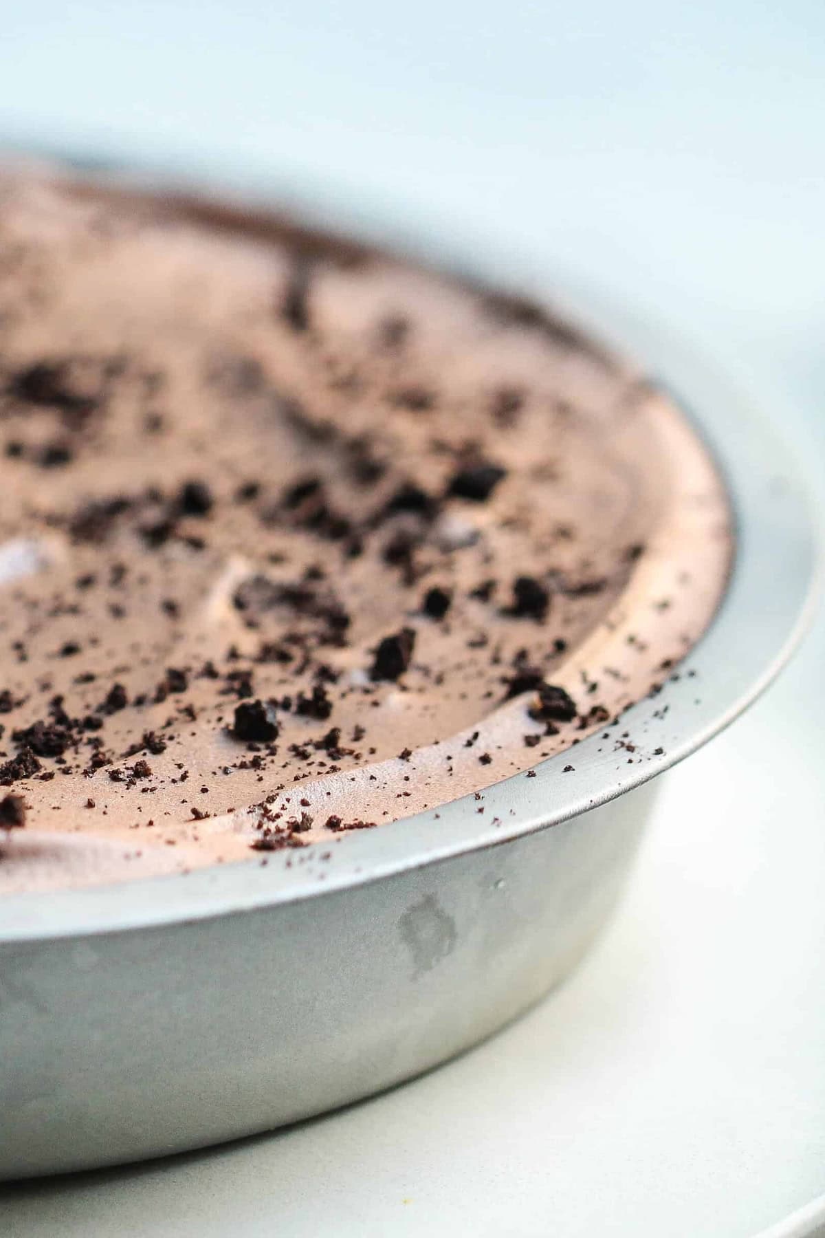 A close-up of a chocolate oreo pie topped with crumbled bits in a round metal pan on a light background.